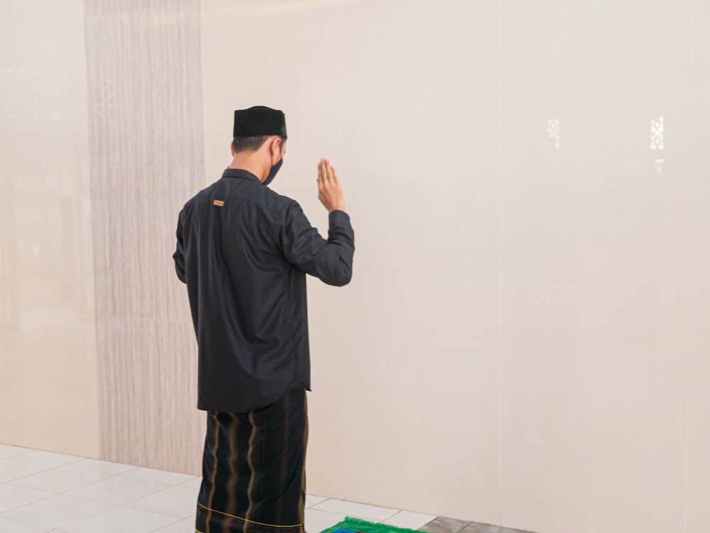 man in black jacket standing near white wall