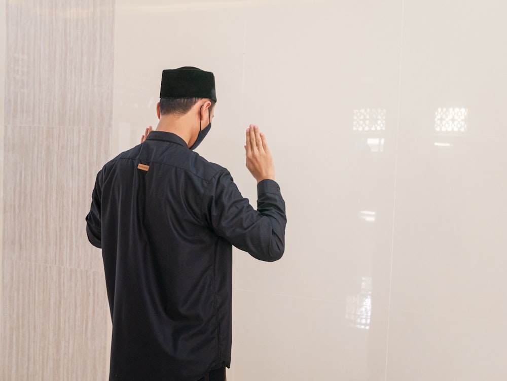 man in black long sleeve shirt standing near white wall