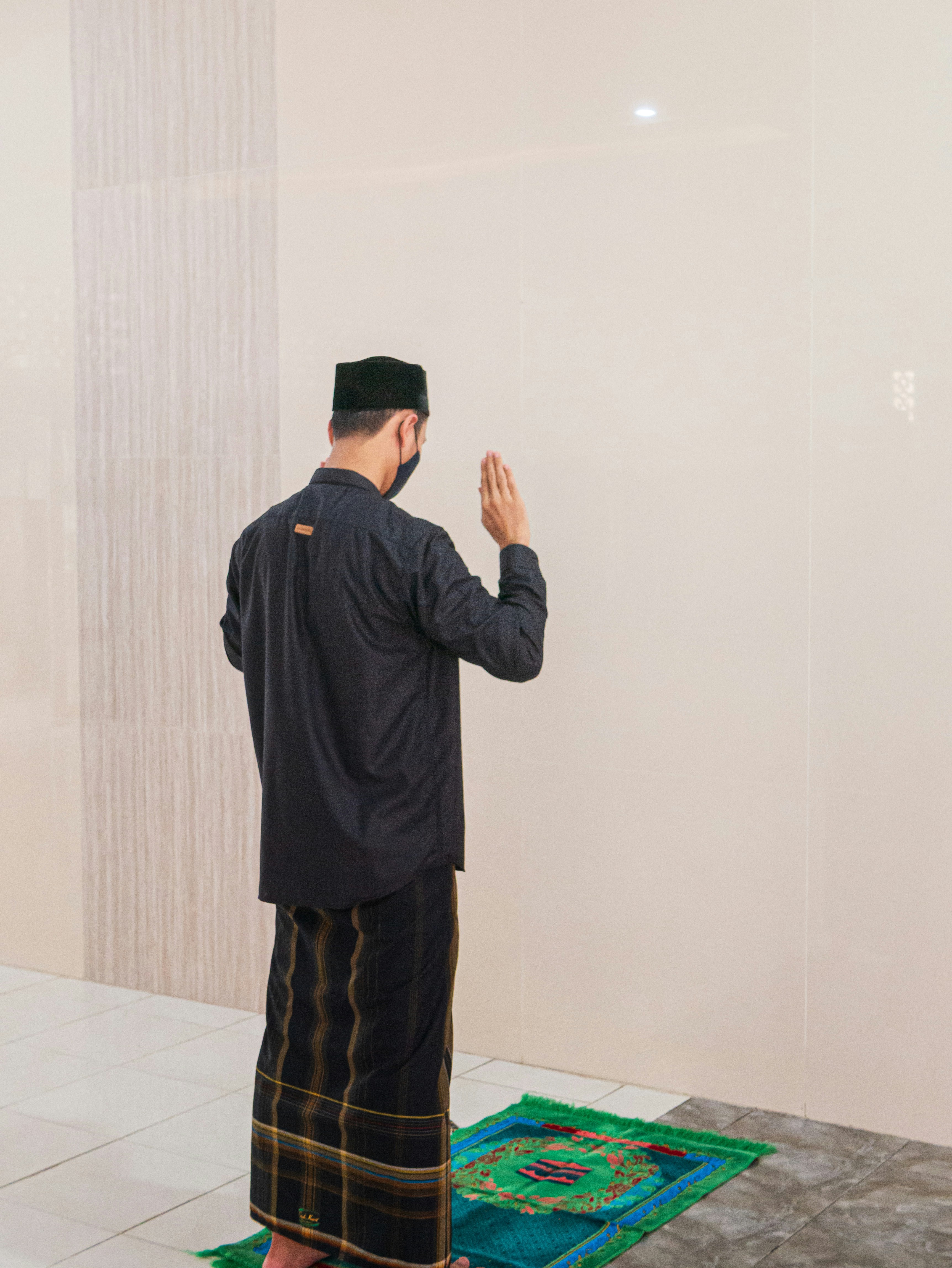 Pria berjaket hitam berdiri di dekat dinding putih