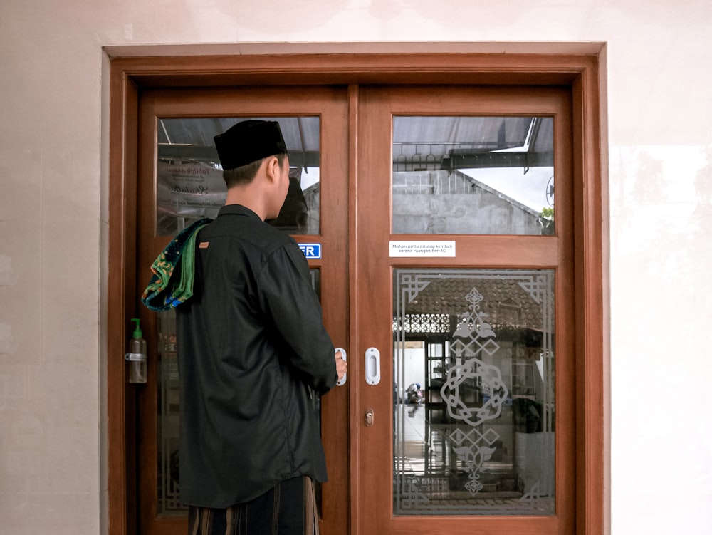 hombre con chaqueta negra de pie frente a la puerta de madera marrón