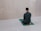 A person is sitting on a prayer mat facing a blank wall in a tiled room. The individual is dressed in a black outfit including a cap. The overall environment appears to be clean and minimalistic.