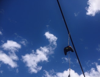 A game controller is hanging from a cable against a backdrop of a bright blue sky with scattered white clouds.