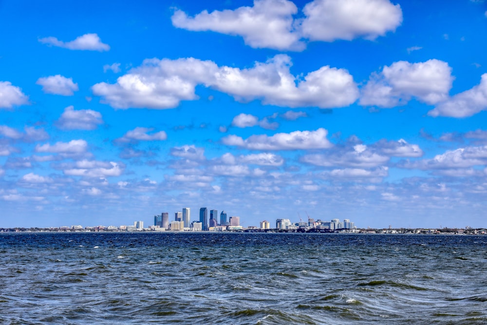 Horizonte de la ciudad a través del cuerpo de agua bajo el cielo nublado soleado azul y blanco durante el día