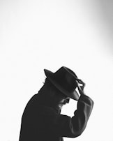 Close-up of a hand adjusting a wide-brimmed hat against a backdrop of city buildings.