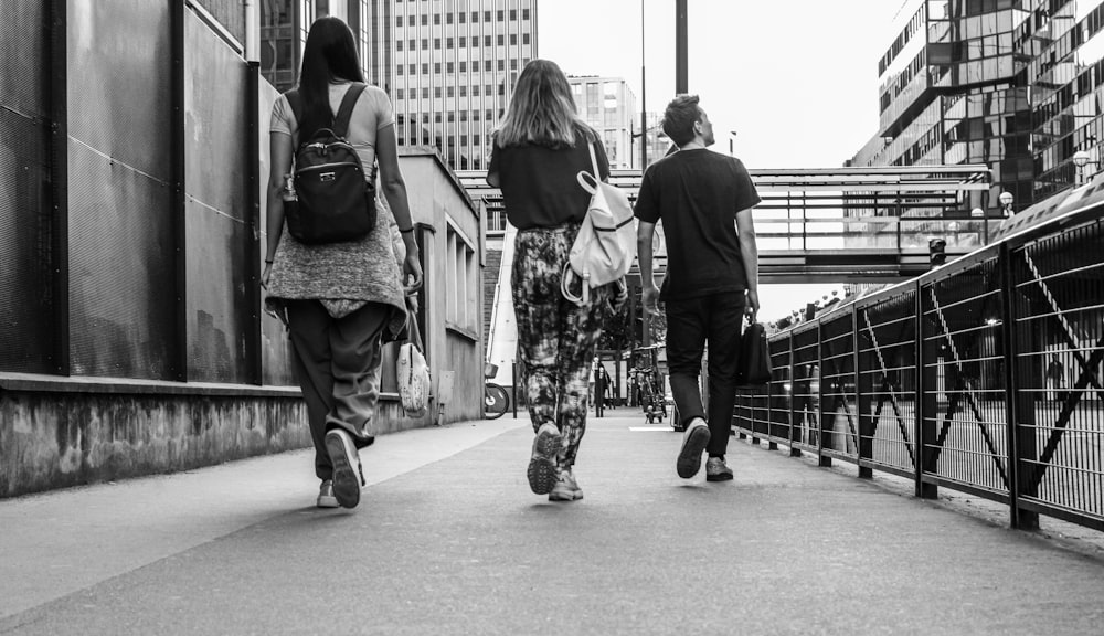 grayscale photo of woman in black jacket and pants carrying backpack walking on sidewalk