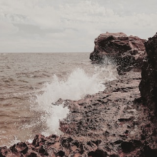Waves crashing energetically onto rugged seaside rocks under a cloudy sky.