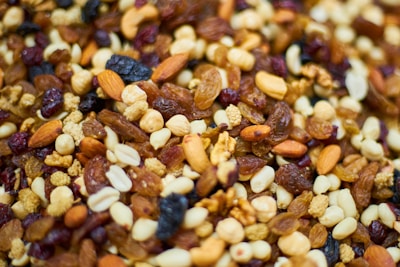 A close-up view of a mixture of nuts and dried fruits. The image includes almonds, walnuts, raisins, cashews, and various other seeds and nuts, with a rich, varied texture.