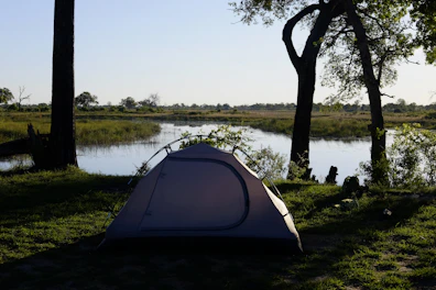 A scenic outdoor scene with a tent pitched near a lake surrounded by pine trees under a clear blue sky.