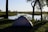 Photo of a green military tent pitched next to a calm lake with forest in the background under a clear sky.