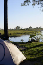 Serene riverside campsite with tents pitched near calm flowing water.