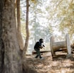 man in black jacket sitting on brown wooden bench near brown trees during daytime