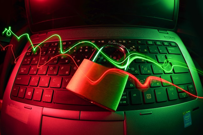 A laptop keyboard is illuminated by red and green light trails, with a padlock placed on top of the keyboard. The lighting creates a dynamic and somewhat futuristic atmosphere, emphasizing themes of security and technology.