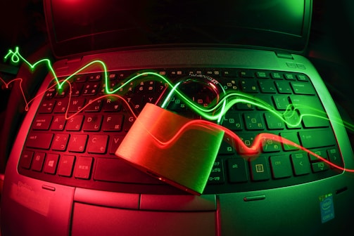 A laptop keyboard is illuminated by red and green light trails, with a padlock placed on top of the keyboard. The lighting creates a dynamic and somewhat futuristic atmosphere, emphasizing themes of security and technology.
