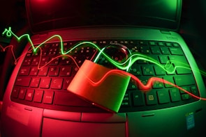 A laptop keyboard is illuminated by red and green light trails, with a padlock placed on top of the keyboard. The lighting creates a dynamic and somewhat futuristic atmosphere, emphasizing themes of security and technology.