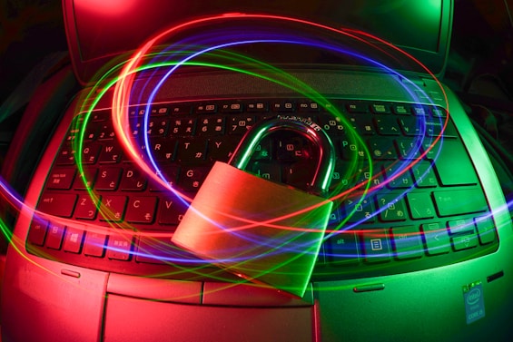 A padlock sits on a laptop keyboard with glowing red, green, and blue light trails swirling around, creating a sense of security and cyber awareness.