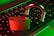 A brass-colored padlock is open, resting on the keyboard of a laptop. The keyboard has Japanese characters, and the scene is illuminated with green and red lighting, creating a dramatic contrast.