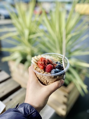 Hands holding a bowl of natural, healthy snack pieces outdoors.
