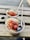 Two bowls of granola are on a wooden table. Each bowl is topped with sliced bananas, fresh blueberries, dried fruits, and chia seeds. Wooden spoons are placed in each bowl.