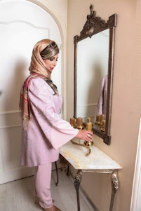A radiant woman in her early 30s adjusting a chic pastel athleisure top in front of a minimalist arch mirror, bathed in warm natural light within an elegant modern home.