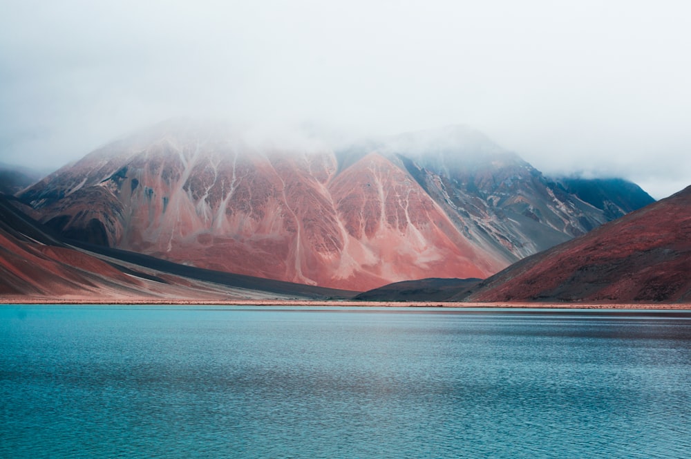 Braune und weiße Berge neben blauem Meer unter weißem Himmel tagsüber