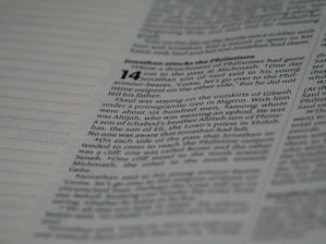 A close-up photo of a person reading an old Hindi manuscript under natural sunlight, highlighting the texture of the paper.