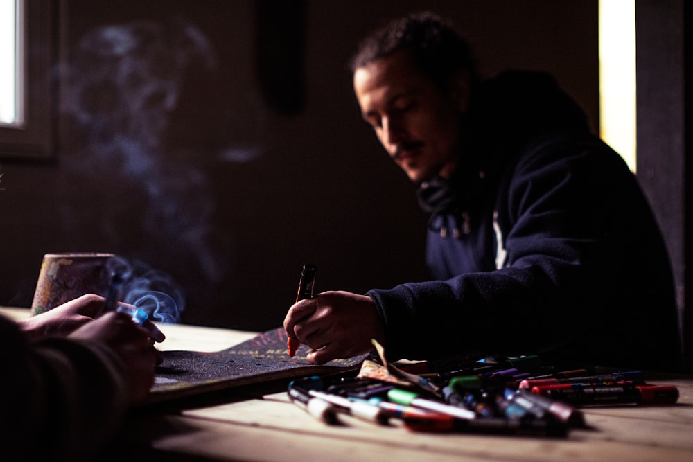 man in black jacket holding pen writing on white paper