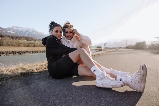 2 women sitting on gray concrete road during daytime