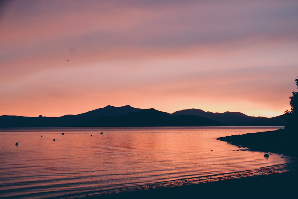 silhouette of mountain near body of water during sunset