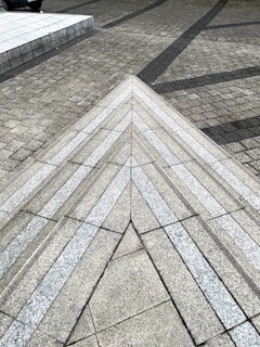 A geometric pattern formed by textured pavement with triangular and linear designs. The surface is made of arranged stone tiles, creating a visually intriguing perspective. Tension between textures and angles adds depth and motion.