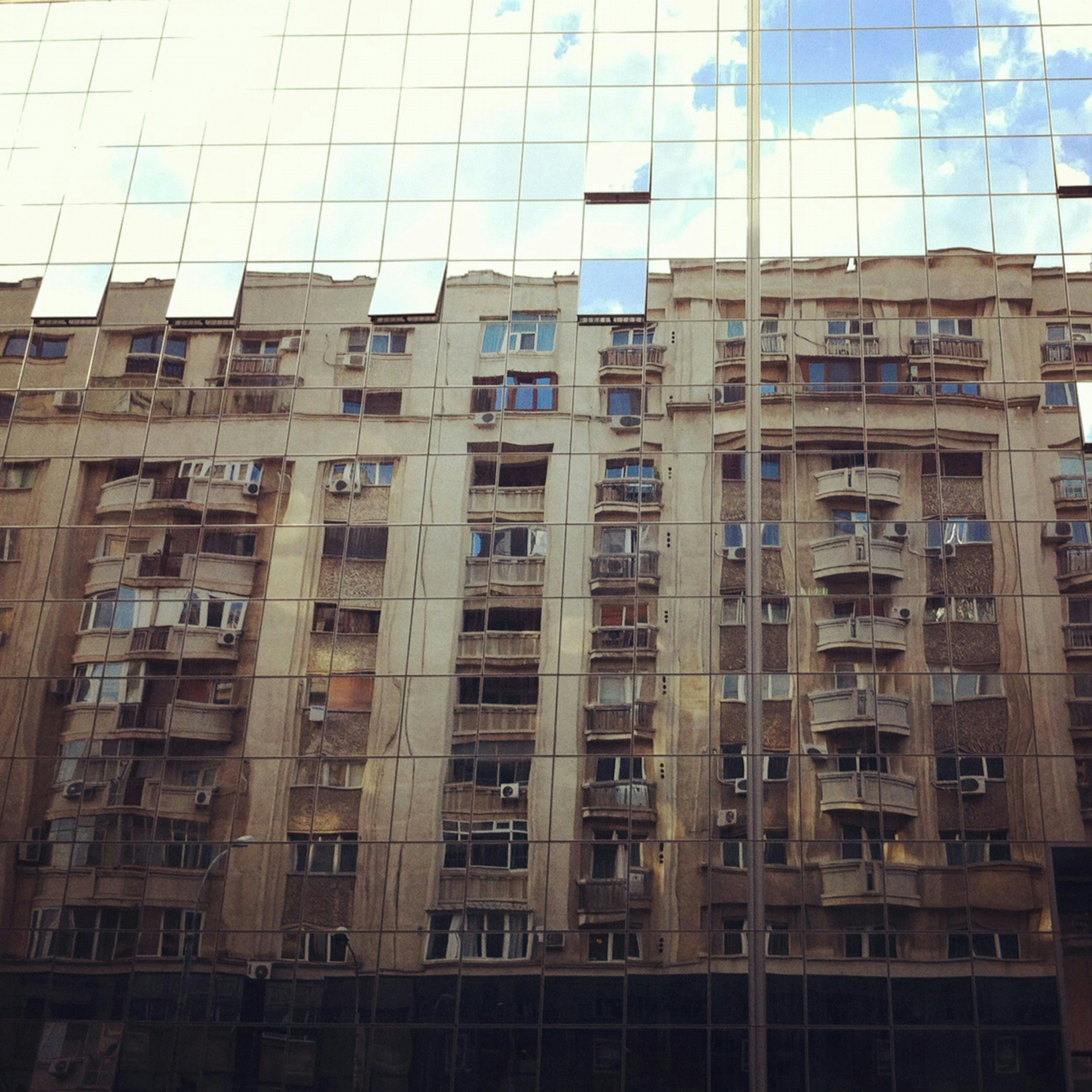 An old apartment building being mirrored in a new building.