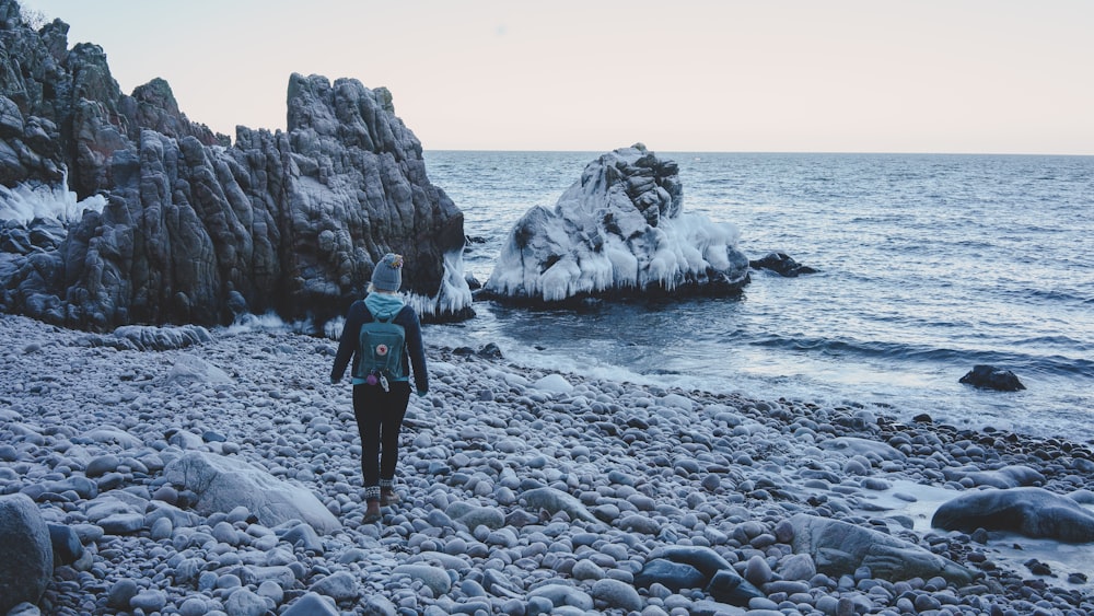 woman in black jacket standing on rocky shore during daytime