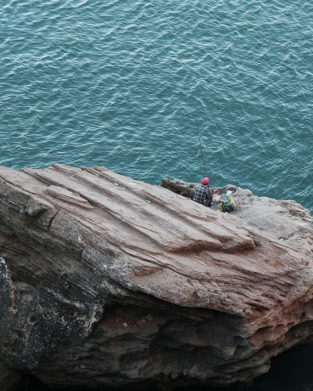 日中、水域近くの茶色の岩の上に座っている緑色のシャツを着た人