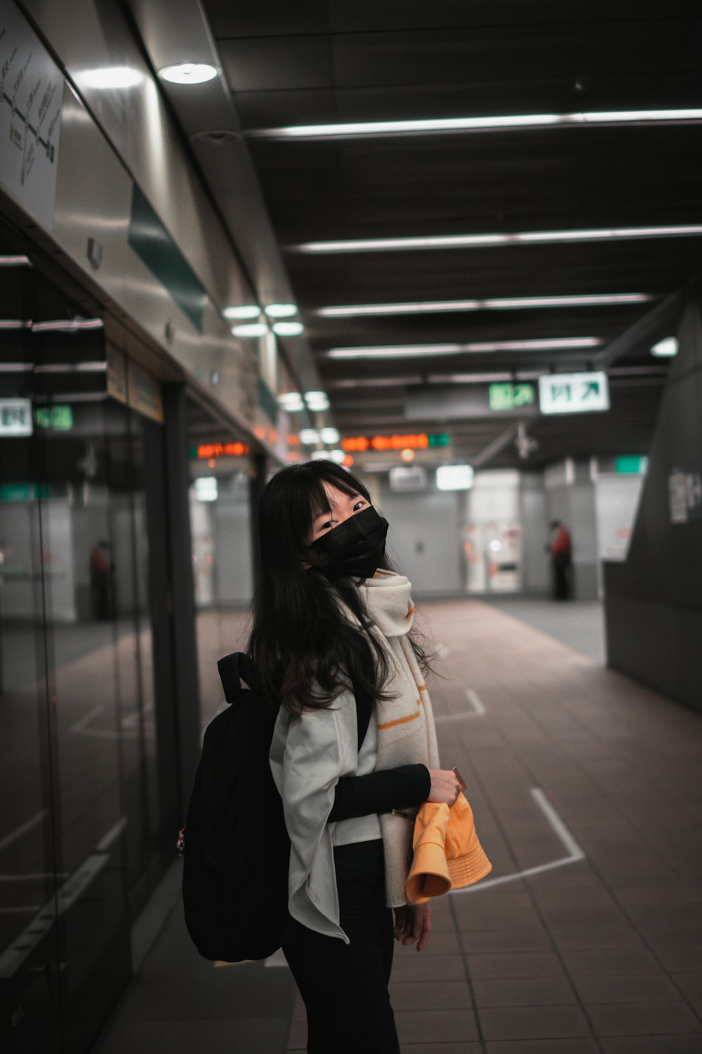 Mujer con chaqueta negra y mochila blanca de pie en la estación de tren