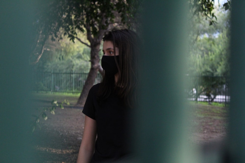 femme en t-shirt noir debout près de l’arbre vert pendant la journée