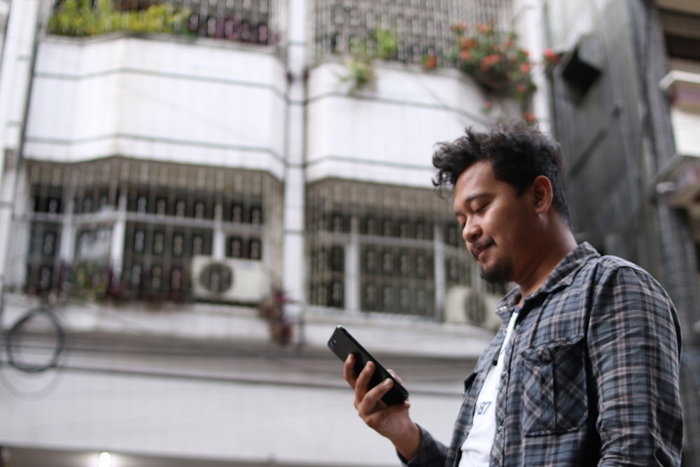 homme en chemise à carreaux bleu et blanc tenant un smartphone noir