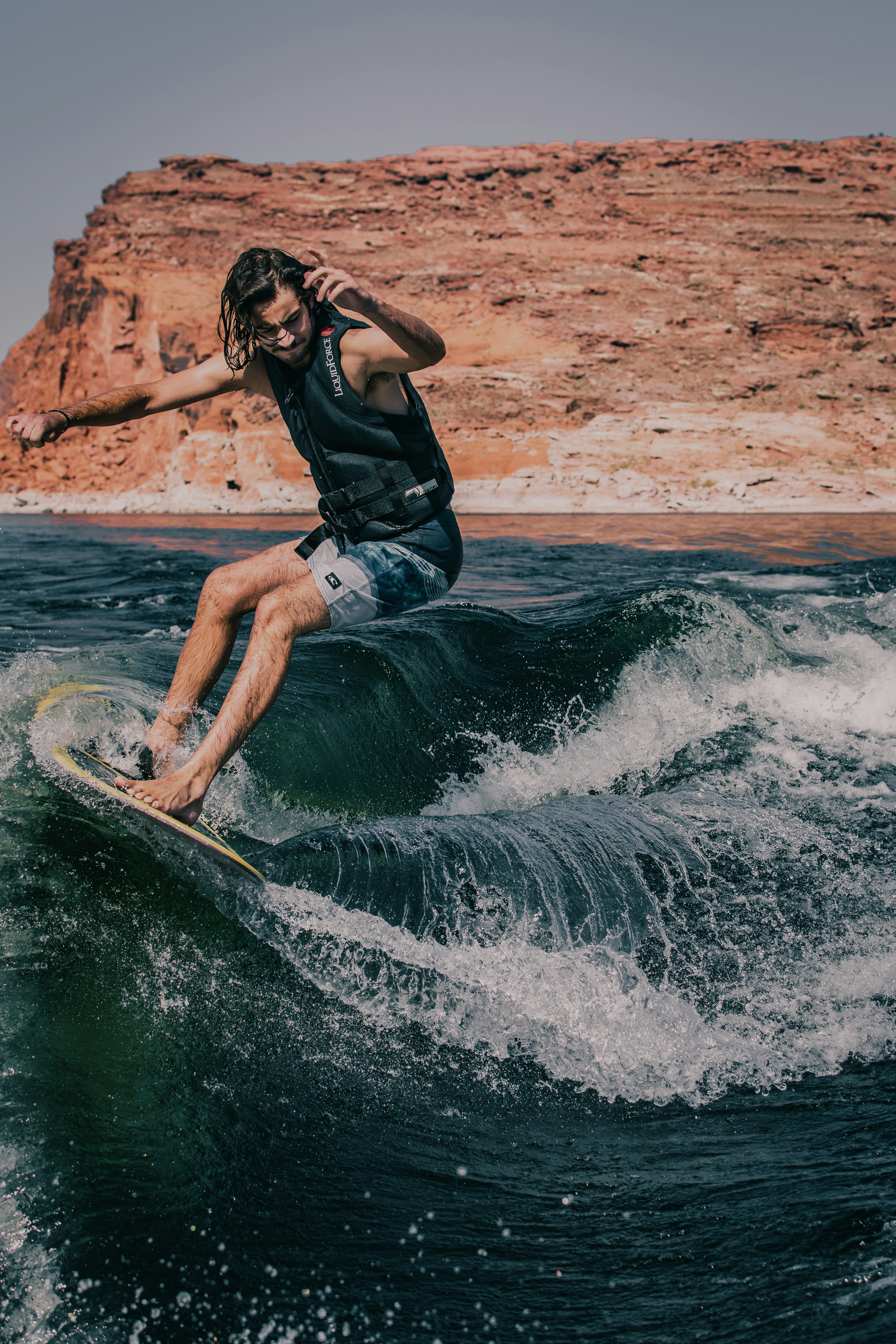 A person surfing in dark blue water. In the background, there is a brown stony cliff.