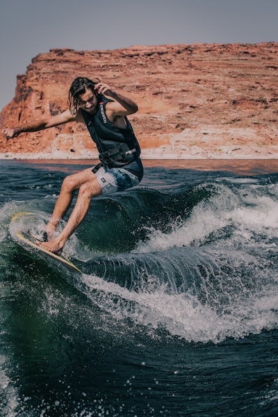 A person surfing in dark blue water. In the background, there is a brown stony cliff.