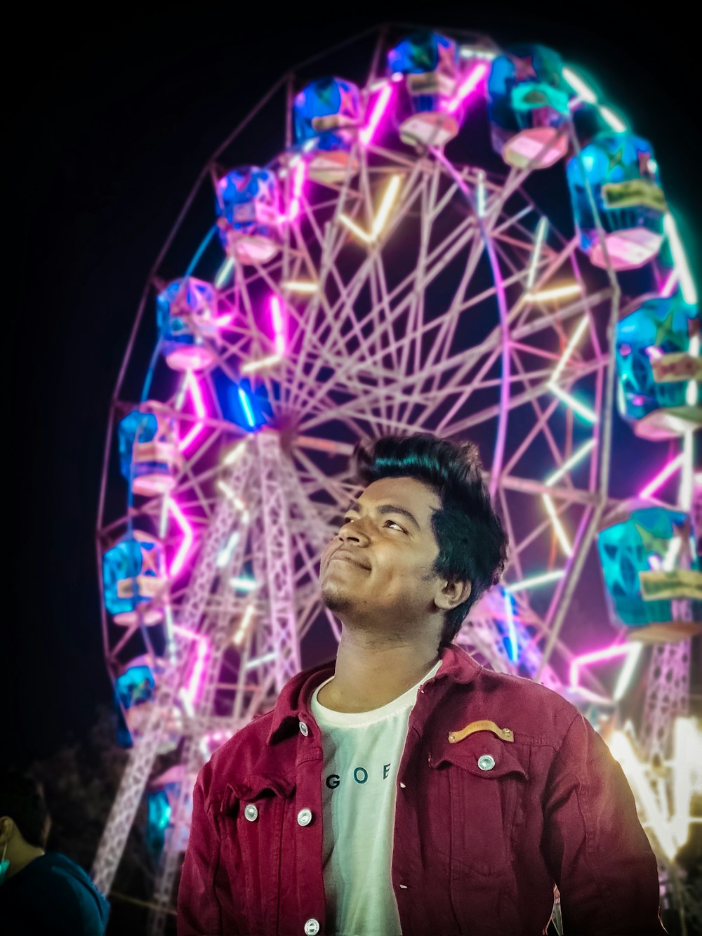 man in pink and white floral shirt standing near ferris wheel