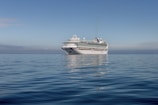 A luxury cruise ship sailing on clear blue ocean waters under a sunny sky.