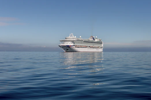 A vibrant cruise ship sailing on turquoise waters under a bright sunny sky with joyful passengers on deck.