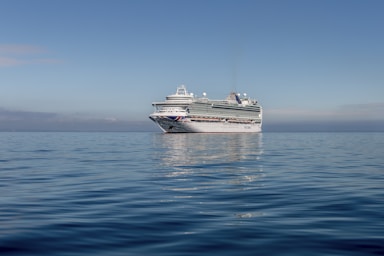 A vibrant cruise ship sailing under a clear blue sky with turquoise Caribbean waters surrounding it.