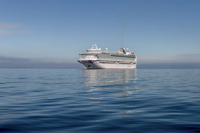 A majestic cruise ship cutting through calm blue waters under a clear sky.