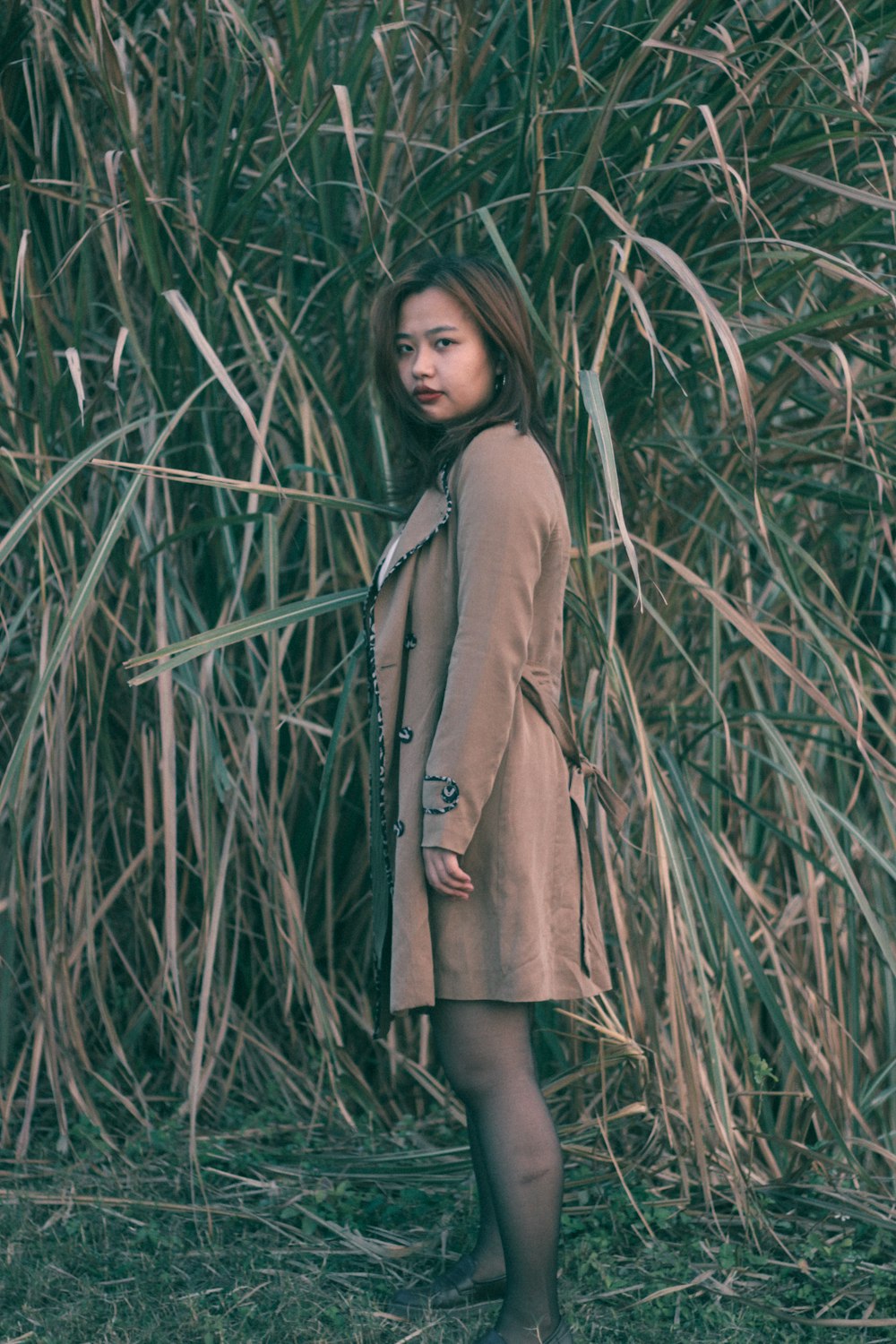 girl in brown coat standing on green grass during daytime