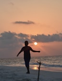 Sunset silhouette of a person walking along the beach wearing a stylish agohha cover-up.