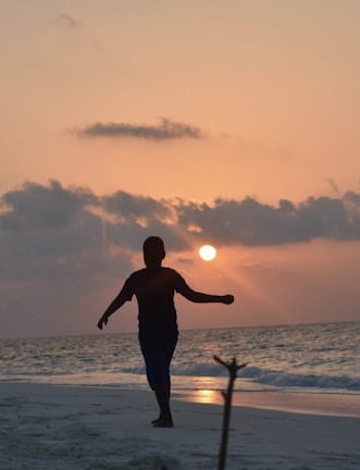 Sunset silhouette of a person walking along the beach wearing a stylish agohha cover-up.