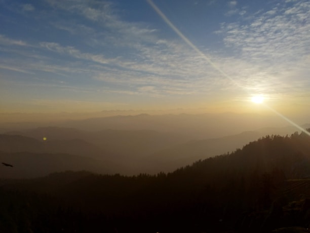 A scenic mountain crest view at sunrise with gentle mist over the landscape.