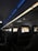 An interior view of an airplane cabin featuring several rows of seats. Each seat is equipped with a personal screen displaying a welcome message and an image of rock formations at sunset. The lighting is dim with a blue ambiance from the overhead compartments.