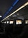 An interior view of an airplane cabin featuring several rows of seats. Each seat is equipped with a personal screen displaying a welcome message and an image of rock formations at sunset. The lighting is dim with a blue ambiance from the overhead compartments.