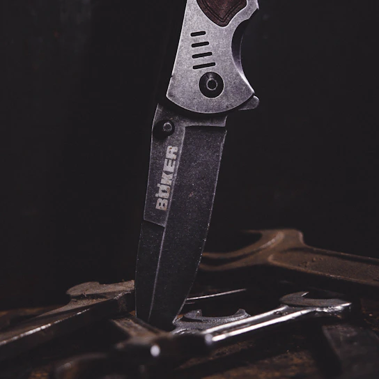Close-up of a sleek stainless steel surgical instrument resting on a parchment-colored surface with a subtle deep crimson background.