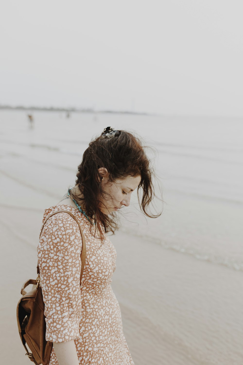 woman in white and brown floral long sleeve shirt standing on white sand during daytime